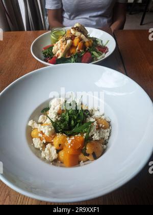 Kürbisgnocchi mit Käse und Rucola und Salat mit Halloumi-Käse, Tomaten. Mahlzeiten werden in einem Restaurant serviert Stockfoto