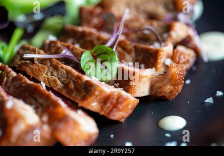 Rindersteak mit Käsesauce und Salat auf einem schwarzen Teller. Selektiver Fokus. Stockfoto