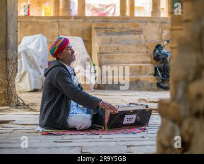 Jaisalmer, Indien - 24. Dezember 2022: Unidentifizierte Nomaden singen und spielen Harmonium im Ghadisar Lake in Jaisalmer, Indien. Harmonium, uralter Instr Stockfoto