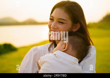 Liebevolle Mutter hält und trägt ihr Neugeborenes in einem öffentlichen Park Stockfoto