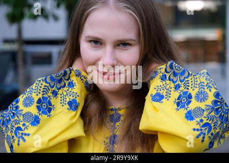 Ein gelbes Hemd mit blauen Blumen und einem wunderschönen jungen Mädchen. Lächelnde Frau schaut in den Rahmen blaue Augen ukrainische Flagge der Ukraine in der Farbe der Kleidung Stockfoto