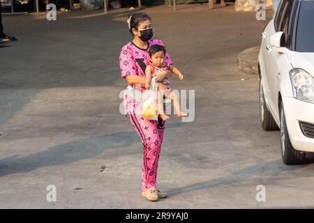 SAMUT PRAKAN, THAILAND, 03 2023. MÄRZ, eine Frau trägt ein Baby auf einer Straße mit einem Marktplatz Stockfoto