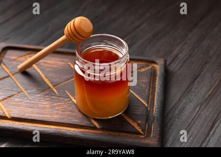 Honig in einem Becher und ein Holzdipper auf einem dunklen Holzbrett auf einem strukturierten Hintergrund. Buchweizenhonig auf dunklem Hintergrund. Stockfoto