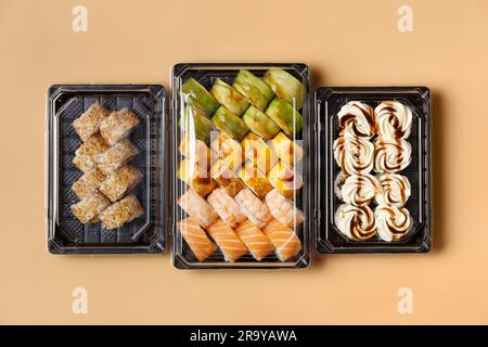 Ein großer Satz Sushi-Brötchen in Plastikpaketen zum Mitnehmen auf hellem Hintergrund. Brötchen mit Lachs, Garnelen, Avocado, Frischkäse, Blick von oben. Stockfoto