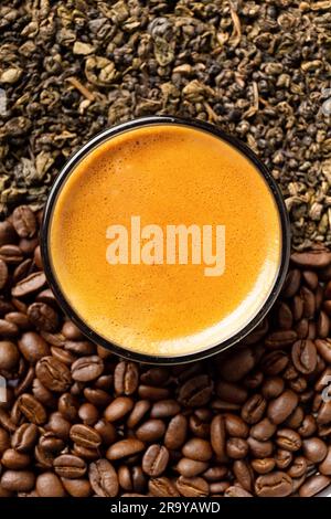 Zusammensetzung von trockenen grünen Teeblättern, gerösteten Kaffeebohnen in einer runden Box und Kaffee in einer Tasse auf dunklem Holzhintergrund Nahaufnahme von oben. Stockfoto