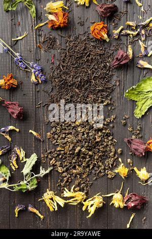 Zusammensetzung von trockenem schwarzem und grünem Tee, Minzblättern und trockenem Hibiskus, Kalendula, Lavendelblumen auf dunklem Holzhintergrund, Nahaufnahme von oben. Stockfoto