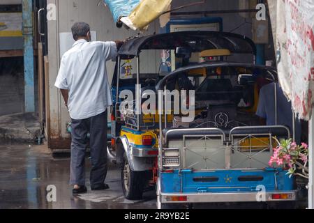 Ein dreirädriger Taxifahrer wischte das Dach des Tuk Tuk vom Regen, Thailand Stockfoto