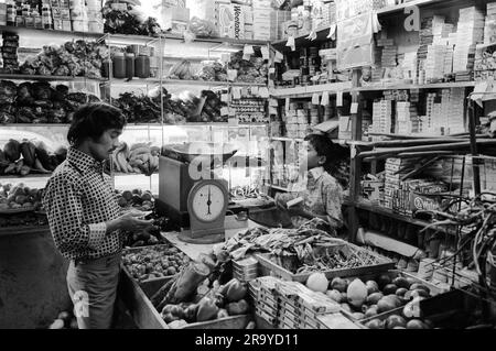 Ein asiatischer Supermarkt in der Brick Lane. Ein kleiner Junge, der einen Kunden in einem familiengeführten Geschäft bedient. Whitechapel, London, England, 1975 1970er Jahre HOMER SYKES Stockfoto