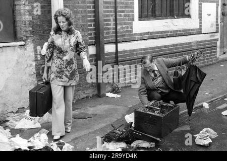 1970er Jahre East End London, Brick Lane. Ein Mann, der nach Transistorradios sucht, und eine gut gekleidete Frau mit einem Koffer, den sie gerade am Ende des Sonntagsmarktes gefunden hat. Tower Hamlets, London, England um 1978. HOMER SYKES AUS DEN 1970ER JAHREN Stockfoto