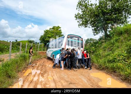 Eine Gruppe junger Leute, die einen Bus schubsen, der auf einer schlammigen Straße feststeckt. Kolumbien, Südamerika. Stockfoto