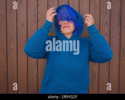 Eine Frau trägt einen hellblauen Hoodie und Jeans in Übergröße. Blauhaarige Frau draußen im Park am Strand von Antalya. Kleidungsmodell, leerer Platz für Text o des Stockfoto