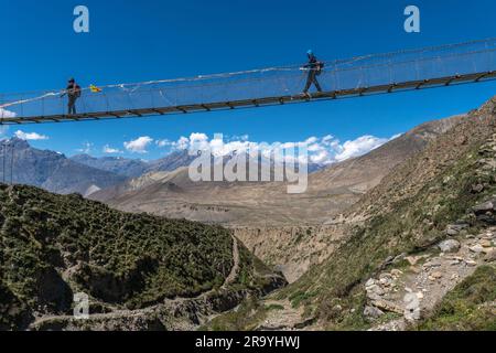 Wanderer, Menschen, die auf einer Hängebrücke über eine tiefe Schlucht reisen, vor einem Hintergrund mit klarem Himmel und schneebedeckten Bergen, Gandhaki Stockfoto