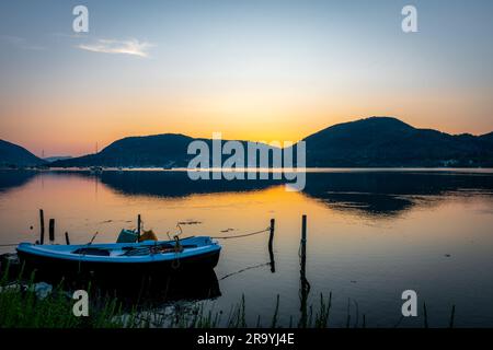 Eine lange Sonnenaufgang-Meereslandschaft mit einem kleinen Holzboot in einer Bucht. Stockfoto