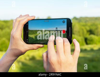 Handaufgenommene Videoaufnahmen auf Handykamera, grünes Sommerlandschaftsbild auf dem Bildschirm. Stockfoto