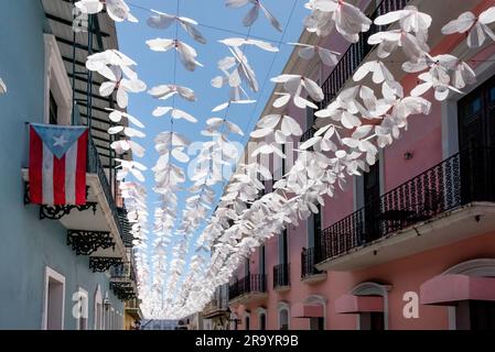 Calle Fortaleza (ehemals Schirmstraße) in der Altstadt von San Juan Puerto Rico mit weißen Schmetterlingstrainern über dem Kopf und Flagge; beliebtes Touristeneinkaufsviertel Stockfoto