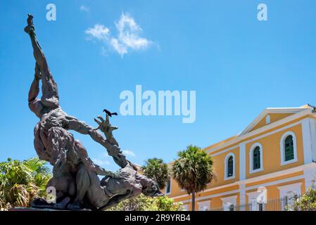 Ballaja Skulptur im Freien in Old San Juan Puerto Rico mit hellgelbem Gebäude und blauem Himmel dahinter. Ein Vogel ruht auf dem Finger einer Figur. Stockfoto