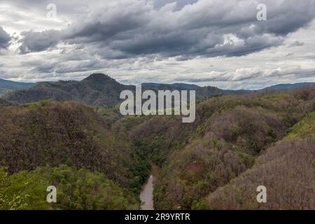 Kleiner, wolkiger Fluss, der zwischen tropischen Dschungelwäldern im Norden Thailands fließt. Wunderschöne Berglandschaft mit dramatischen Wolken. Kleines Boot im jun Stockfoto