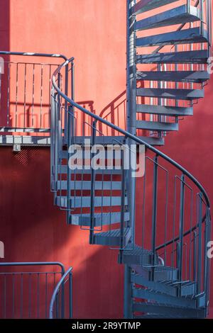 Treppe und Schatten. Graue Metalltreppe neben der Wand des orangefarbenen Gebäudes. Stockfoto