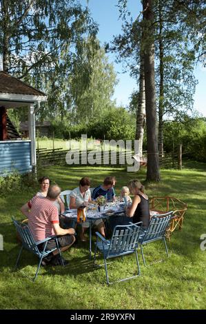 Die Familie isst draußen auf dem Rasen des Sommerhauses auf dem Land. Dalarna, Schweden. Stockfoto