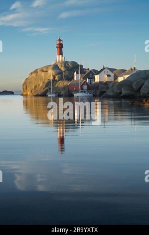 Leuchtturm auf Felsen in einem Abstand mit Reflexion im ruhigen und friedlichen Meer Stockfoto