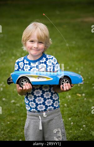 Porträt eines süßen und glücklichen kleinen Jungen, der draußen ein ferngesteuertes Auto hält Stockfoto