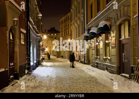 Mann, der nachts auf der Österlånggatan Straße in der Altstadt zwischen Gebäuden spaziert Stockfoto