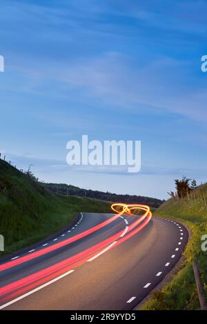 Helle Pfade fahrender Fahrzeuge auf der Landstraße vor blauem Himmel. Skane, Schweden. Stockfoto