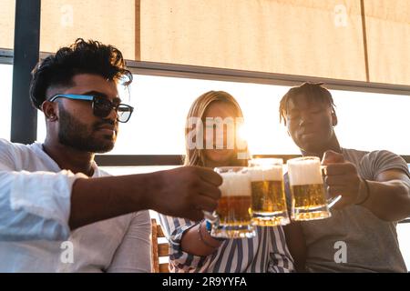 Kleine Gruppe von jungen erwachsenen multiethnischen Freunden, die mit drei Tassen Bier anstoßen - Sommerferienkonzept auf einem Schiff auf dem Fluss Stockfoto