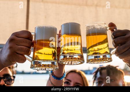 Kleine Gruppe von jungen erwachsenen multiethnischen Freunden, die mit drei Tassen Bier anstoßen - Sommerferienkonzept auf einem Schiff auf dem Fluss Stockfoto