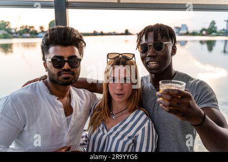 Kleine Gruppe von jungen erwachsenen multiethnischen Freunden, die mit Alkohol anstoßen - Sommerferienkonzept auf einem Schiff auf dem Fluss Stockfoto