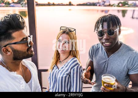 Kleine Gruppe von jungen erwachsenen multiethnischen Freunden, die mit Alkohol anstoßen - Sommerferienkonzept auf einem Schiff auf dem Fluss Stockfoto