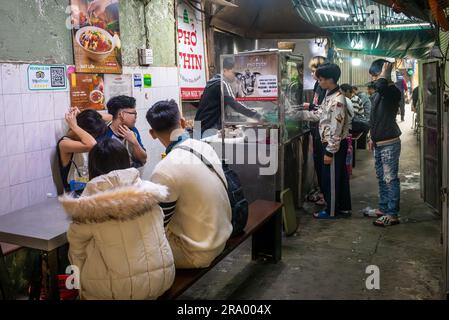 Junge Leute warten in Pho Thin auf ihre traditionellen Schüsseln Pho oder Nudelsuppe in Hanoi, Vietnam. Pho kann zu jeder Tageszeit gegessen werden Stockfoto
