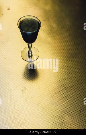 Schwarzes Holzkohle-Limonade-Getränk in schillerndem Sherry-Glas auf goldenem Messingtisch, Sommerabend im Freien Stockfoto