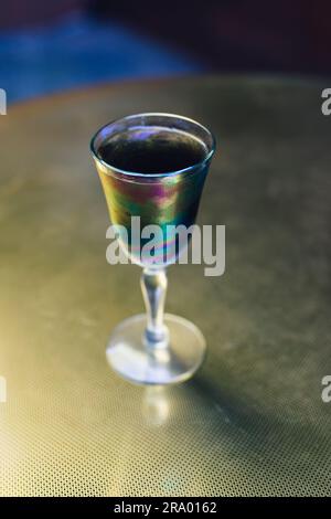 Schwarzes Holzkohle-Limonade-Getränk in schillerndem Sherry-Glas auf goldenem Messingtisch, Sommerabend im Freien Stockfoto