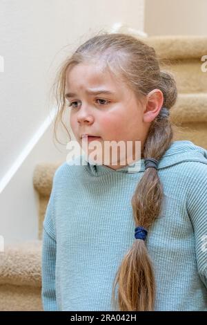 Porträt eines sehr unglücklichen 7-jährigen Mädchens, das auf einer Treppe sitzt. HERR Stockfoto