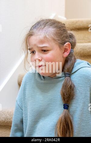 Porträt eines sehr unglücklichen 7-jährigen Mädchens, das auf einer Treppe sitzt. HERR Stockfoto