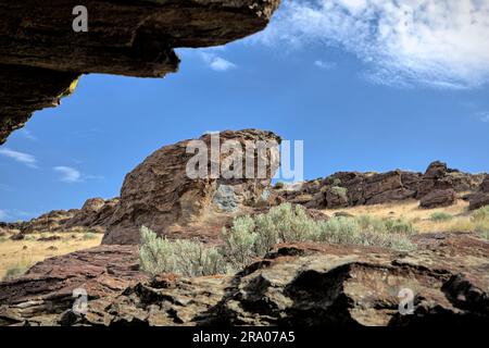 Blick von einer kleinen Höhle auf große Felsen und trockene Bürsten vor einem hellen und klaren Himmel in der Nähe von Buhl, Idaho. Stockfoto