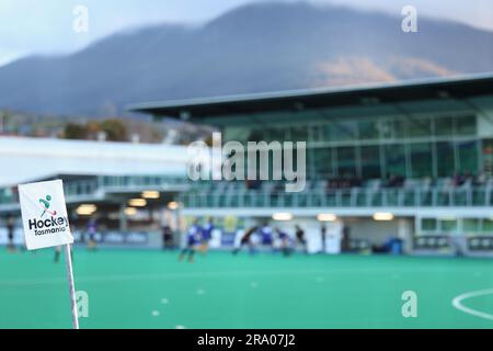 Eine Flagge auf einer Stange mit sichtbarem Hockey Tasmania Logo. Mt. Wellington (Kunanyi) im Hintergrund mit absichtlich verschwommenem Stadion, Spielern und Werbern Stockfoto