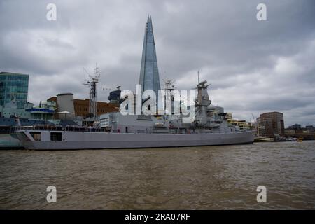 Ein modernes Militärschiff, das neben HMS Belfast mit The Shard im Hintergrund vertäut ist Stockfoto