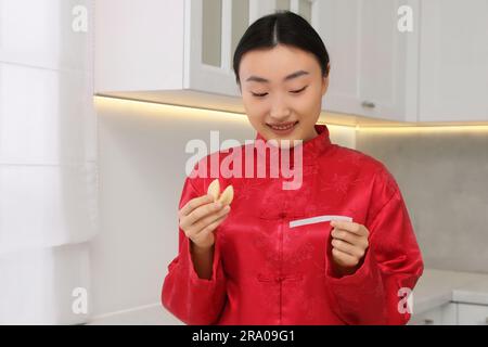 Asiatische Frau hält leckeren Glückskeks mit Vorhersage in der Küche. Platz für Text Stockfoto