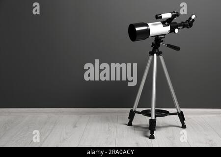 Stativ mit modernem Teleskop nahe der grauen Wand. Platz für Text Stockfoto