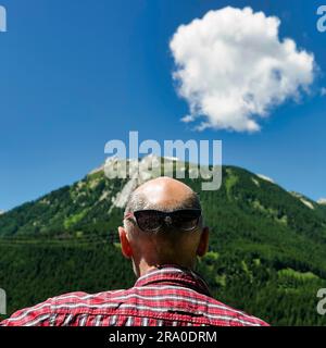 Lustiges surreales Porträt, Bestes Alter mit Glatze und Sonnenbrille auf dem Hinterkopf, Blick auf die Alpen, Blick von hinten, Schweiz Stockfoto