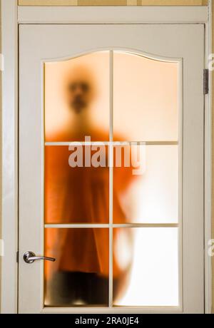 Silhouette von einem unbekannten Mann in Orange durch eine geschlossene Glastür, wie ein Geist oder ein Alien gesehen Stockfoto