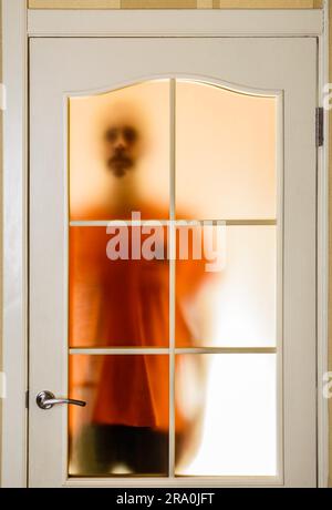 Silhouette von einem unbekannten Mann in Orange durch eine geschlossene Glastür, wie ein Geist oder ein Alien gesehen Stockfoto