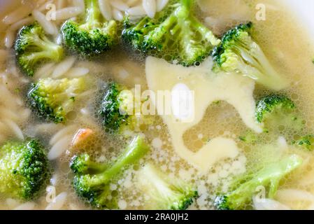 Makroaufnahme einer Suppe mit Brokkoli, Kohl, Reis, Nudeln und butter in warme Hühnerbrühe Stockfoto