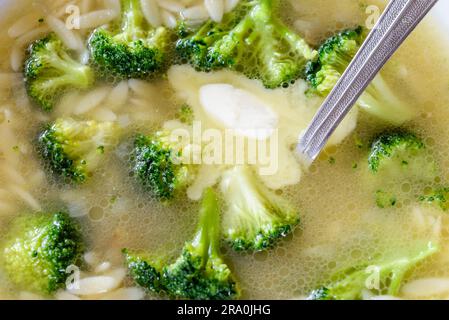 Makroaufnahme einer Suppe mit Brokkoli, Kohl, Reis, Nudeln und butter in warme Hühnerbrühe Stockfoto