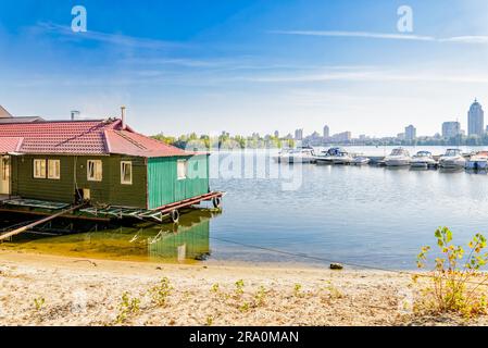 Ein kleines Haus in der Nähe des Flusses. Einige Boote sind geparkt. Die Stadt wird im Hintergrund angezeigt Stockfoto