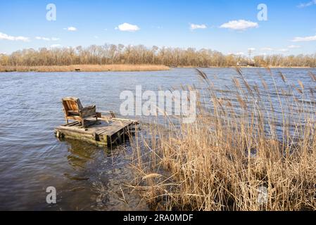 Ein komfortabler Sessel auf einem Ponton wartet auf einen Fischer auf dem See. Die Wolken laufen am blauen Himmel, vom Wind geschoben Stockfoto