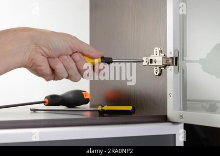 Ein Mann verwendet einen Schraubenzieher, um eine verdeckte Scharnier fest auf einem modernen Schrank mit Glastür anzupassen Stockfoto