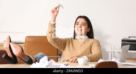 Junge Frau, die Papierflugzeug an den Tisch im Büro wirft Stockfoto